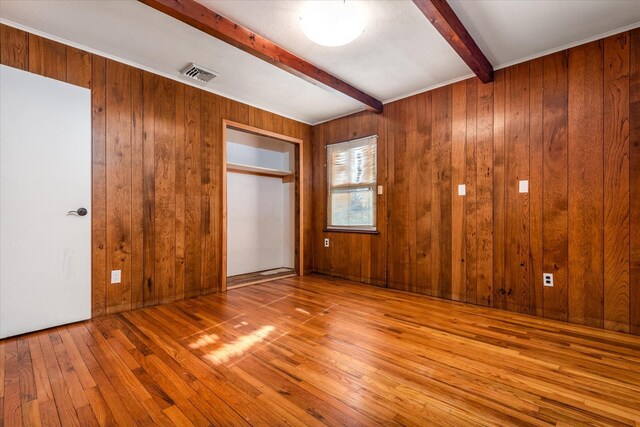 unfurnished bedroom featuring beam ceiling, a closet, visible vents, wooden walls, and wood finished floors