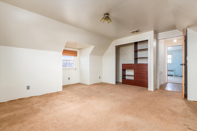 additional living space with radiator, light carpet, vaulted ceiling, and visible vents