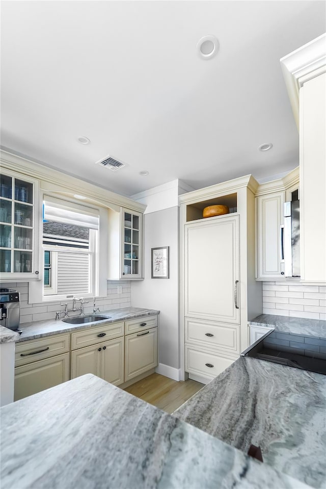 kitchen with sink, light stone counters, cream cabinets, light hardwood / wood-style floors, and decorative backsplash