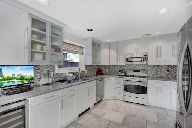 kitchen with sink, backsplash, stainless steel appliances, white cabinets, and beverage cooler