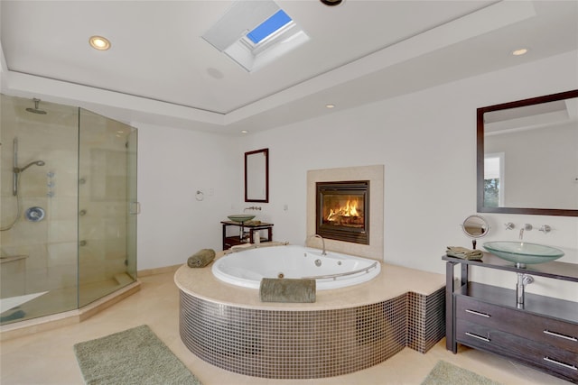 bathroom with a skylight, vanity, a high end fireplace, plus walk in shower, and a raised ceiling