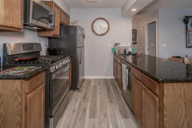 kitchen with stainless steel appliances, light hardwood / wood-style floors, sink, and dark stone counters