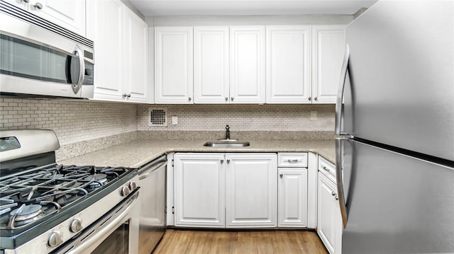 kitchen with appliances with stainless steel finishes, tasteful backsplash, sink, white cabinets, and light wood-type flooring