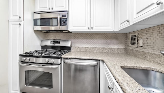 kitchen with white cabinetry, sink, decorative backsplash, stainless steel appliances, and light stone countertops