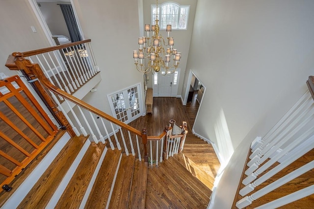 stairway with hardwood / wood-style flooring, a chandelier, and a high ceiling