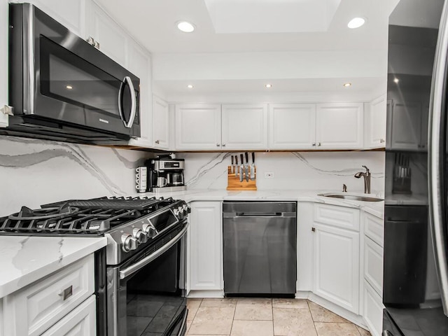 kitchen featuring sink, white cabinetry, light stone counters, black appliances, and backsplash