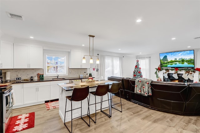 kitchen with stainless steel electric range, a breakfast bar area, hanging light fixtures, white cabinets, and light wood-type flooring