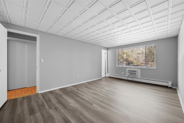 unfurnished bedroom featuring a baseboard radiator, wood-type flooring, and a wall mounted air conditioner