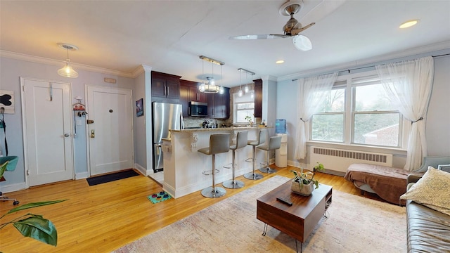 living room with ceiling fan, ornamental molding, radiator heating unit, and light wood-type flooring