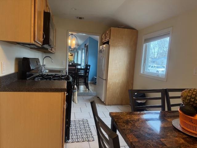 kitchen featuring gas stove, white fridge, light tile patterned floors, and lofted ceiling