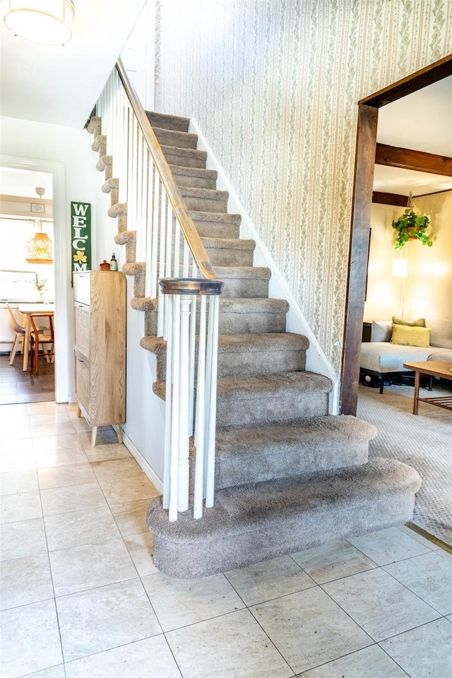 stairway with tile patterned flooring, beam ceiling, baseboards, and wallpapered walls