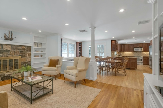 living room with a stone fireplace, light hardwood / wood-style flooring, and decorative columns