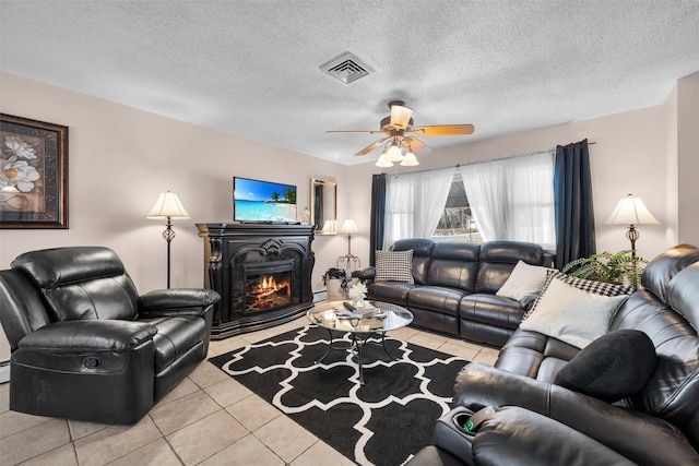 living area featuring visible vents, a ceiling fan, a textured ceiling, tile patterned flooring, and a warm lit fireplace