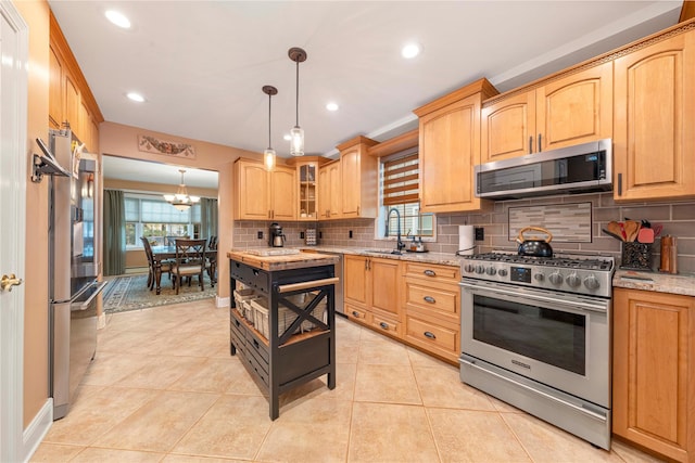 kitchen with sink, stainless steel appliances, light stone counters, decorative backsplash, and decorative light fixtures