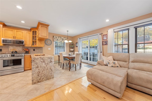 kitchen with tasteful backsplash, hanging light fixtures, light brown cabinets, light hardwood / wood-style flooring, and stainless steel appliances