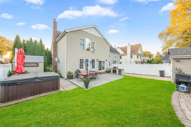 back of house with a hot tub, a patio, and a lawn