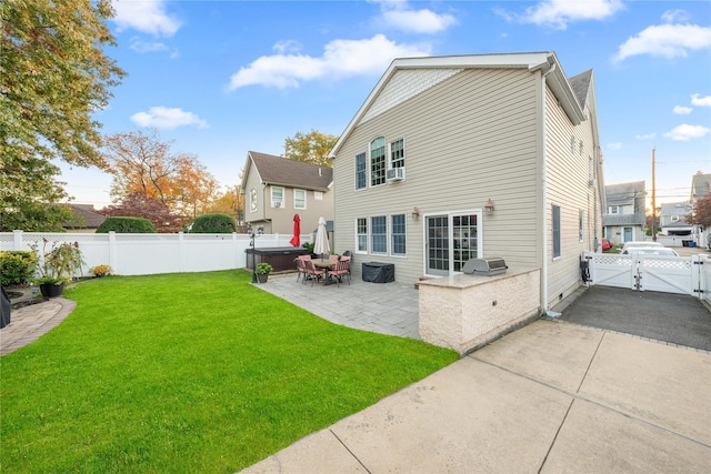 back of house with a hot tub, exterior kitchen, a lawn, and a patio area