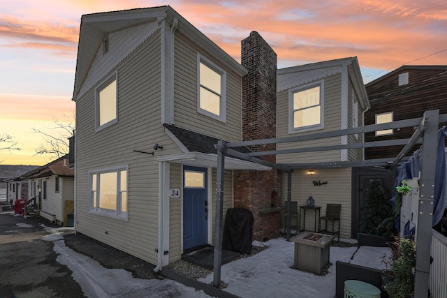 back of property at dusk featuring a fire pit and a chimney