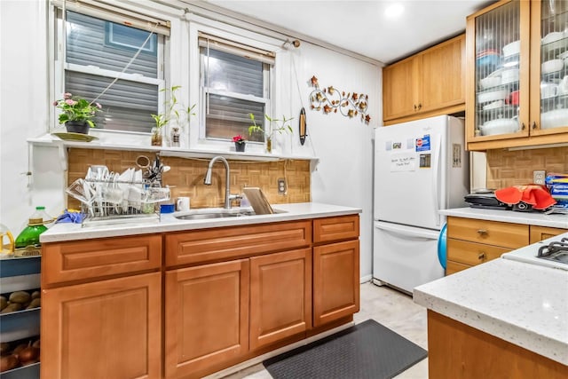 kitchen featuring light stone counters, freestanding refrigerator, a sink, glass insert cabinets, and tasteful backsplash