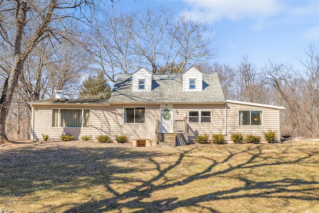 cape cod-style house featuring a shingled roof and a front yard