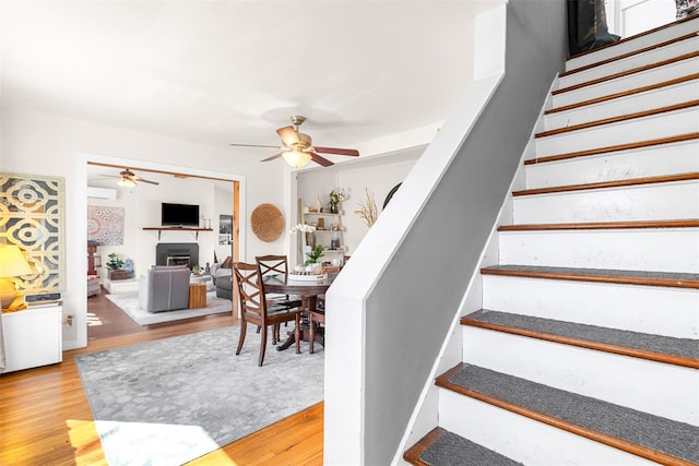 staircase with a fireplace, a ceiling fan, wood finished floors, and a wall mounted air conditioner