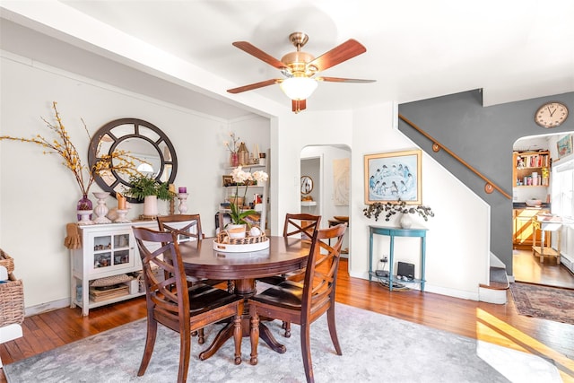 dining room with arched walkways, hardwood / wood-style flooring, ceiling fan, baseboards, and stairs