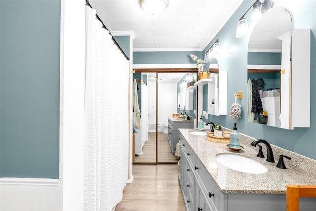 full bathroom featuring wood finished floors, wainscoting, a sink, and crown molding