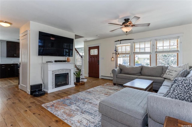 living area with a ceiling fan, light wood-type flooring, a fireplace, and a baseboard radiator