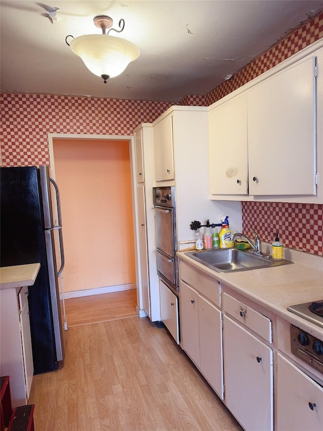 kitchen featuring freestanding refrigerator, white cabinets, light countertops, and a sink