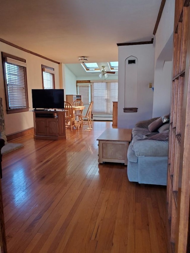 living room with crown molding, a baseboard radiator, wood-type flooring, and a skylight