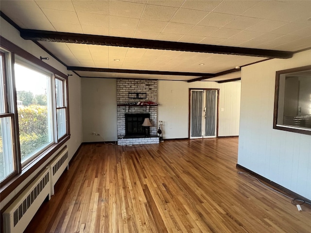 unfurnished living room with hardwood / wood-style flooring, a brick fireplace, radiator heating unit, and beam ceiling