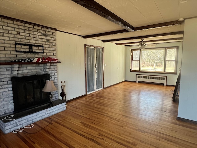 unfurnished living room with radiator heating unit, beam ceiling, hardwood / wood-style floors, and a brick fireplace