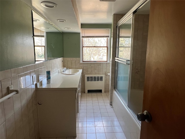 bathroom featuring shower / bath combination with glass door, tile walls, tile patterned flooring, radiator heating unit, and vanity