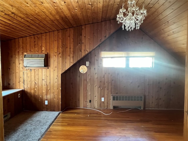 additional living space featuring radiator, hardwood / wood-style floors, a wall mounted air conditioner, vaulted ceiling, and a chandelier