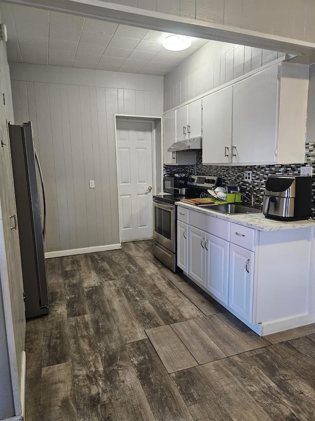 kitchen featuring dark wood-type flooring, under cabinet range hood, backsplash, white cabinetry, and appliances with stainless steel finishes