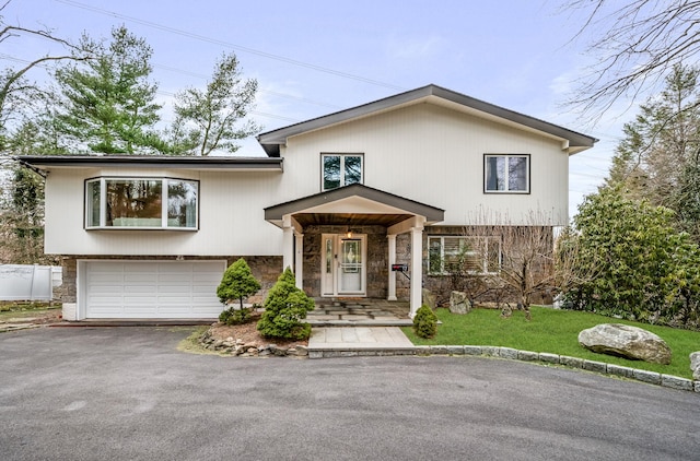 view of front facade featuring aphalt driveway, a front yard, stone siding, and an attached garage