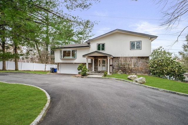 view of front of property with aphalt driveway, a front yard, fence, a garage, and stone siding