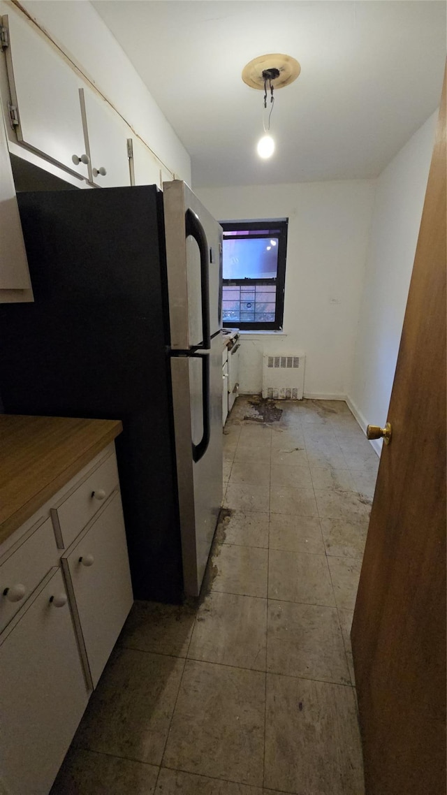 kitchen with white cabinetry, radiator, light tile patterned flooring, and stainless steel refrigerator