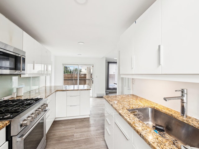 kitchen with appliances with stainless steel finishes, white cabinetry, sink, light stone counters, and light hardwood / wood-style flooring