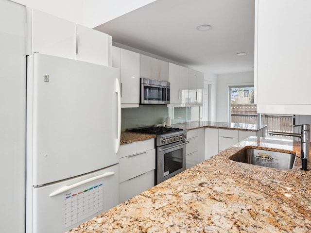 kitchen featuring white cabinetry, appliances with stainless steel finishes, sink, and light stone counters