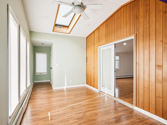 unfurnished room featuring hardwood / wood-style flooring, vaulted ceiling with skylight, baseboard heating, and wood walls