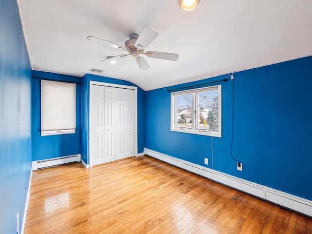 unfurnished bedroom with a closet, lofted ceiling, a baseboard heating unit, and light hardwood / wood-style flooring