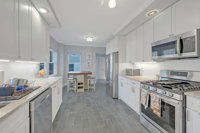 kitchen with light stone counters, ornamental molding, appliances with stainless steel finishes, decorative backsplash, and white cabinets