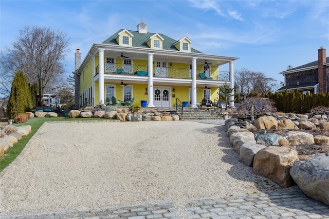 view of front of house featuring a porch, gravel driveway, a balcony, and a ceiling fan