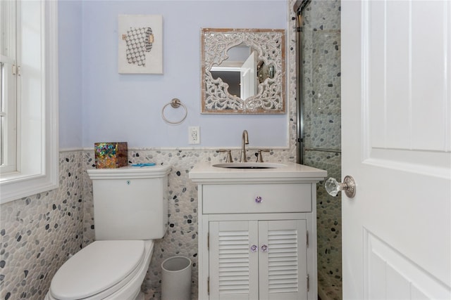 bathroom featuring toilet, wainscoting, vanity, and tile walls