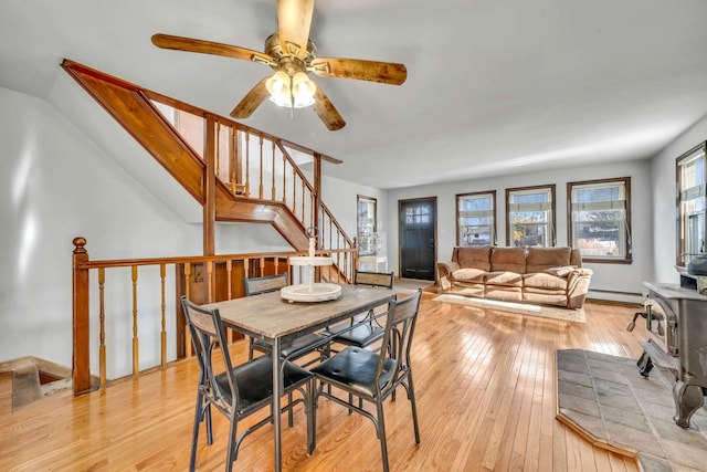 dining room featuring a baseboard radiator, a wood stove, ceiling fan, and light hardwood / wood-style flooring