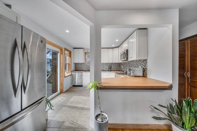 kitchen with light tile patterned flooring, wooden counters, stainless steel appliances, decorative backsplash, and white cabinets