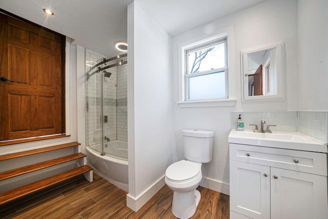 full bathroom with hardwood / wood-style flooring, bath / shower combo with glass door, vanity, decorative backsplash, and toilet