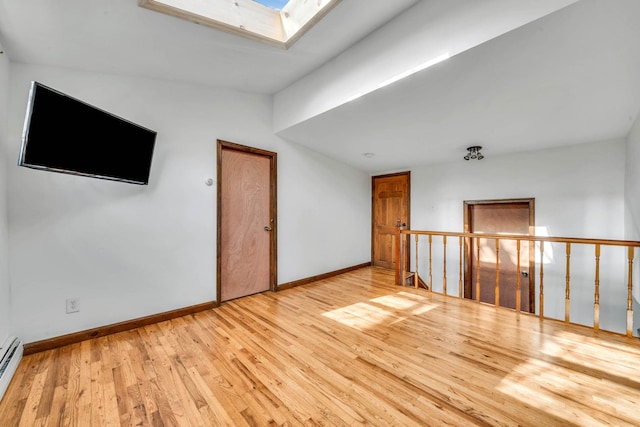 empty room with a skylight, light hardwood / wood-style floors, and a baseboard radiator