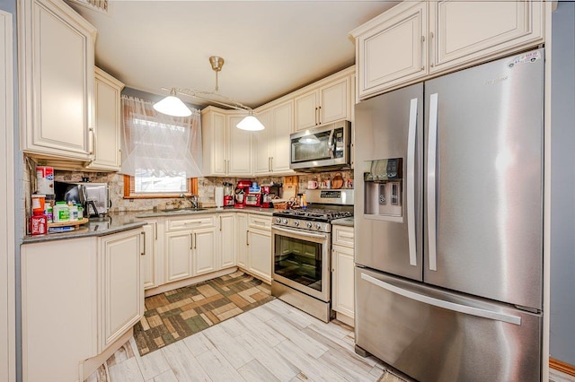 kitchen featuring sink, stainless steel appliances, tasteful backsplash, decorative light fixtures, and cream cabinetry